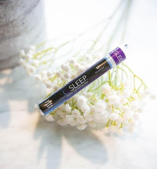 A spray bottle labeled 'SLEEP' positioned on a bed of white flowers, suggesting a calming or sleep-inducing product.